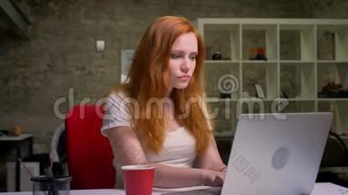 聪明的红发女郎正在笔记本电脑上打字，正满怀信心地看着屏幕，<strong>专心</strong>工作